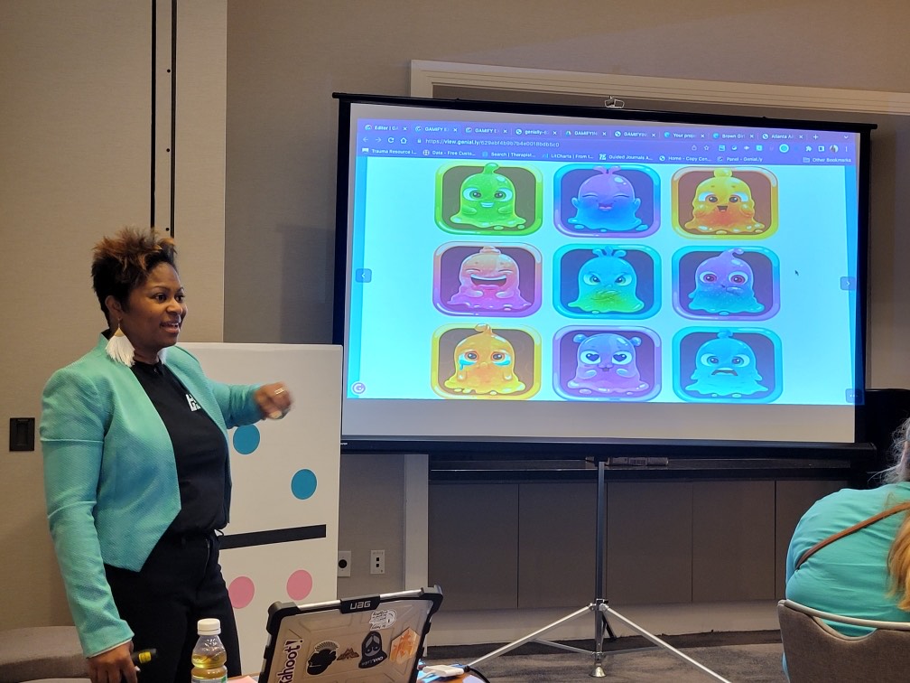 Charell G. Coleman standing at the front of a classroom to the right of a projector screen, facing the audience.